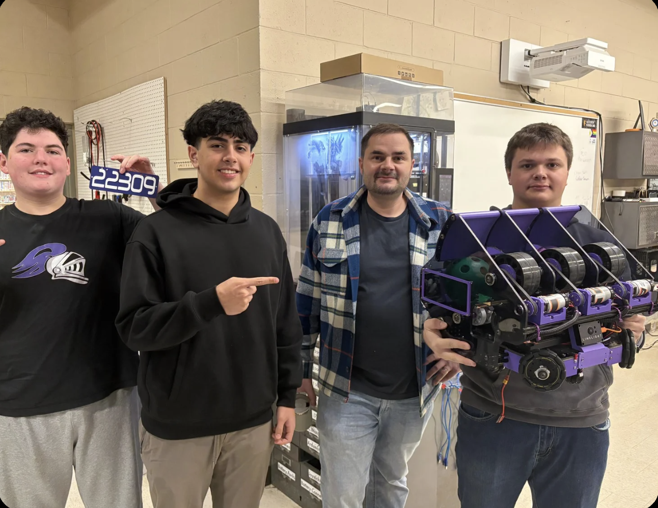 Team members with robot in workshop holding team number sign